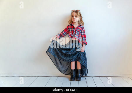 Sweet happy fashion adorable petite fille habillée comme hippie hippie gypsy cowboy dans lunettes standing against white wall background à la lumière Banque D'Images