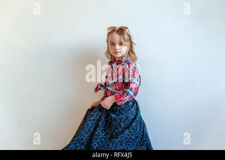 Sweet happy fashion adorable petite fille habillée comme hippie hippie gypsy cowboy dans lunettes standing against white wall background à la lumière Banque D'Images