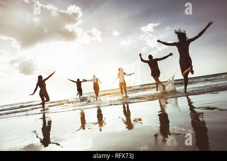 Grand groupe d'amis heureux court et saute de sunset beach. Six silhouettes actives contre mer plage Banque D'Images