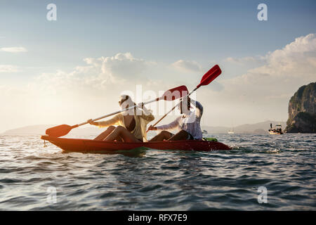 Couple heureux des balades en canoë ou kayak de mer de la baie au coucher du soleil. Kayak ou canot concept avec les gens Banque D'Images