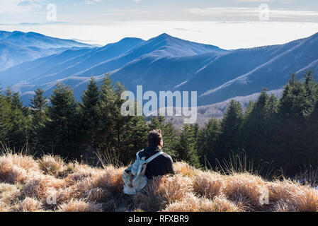 Un homme portant un sac à dos vintage randonneur assis seul à admirer le paysage de montagne en hiver. Banque D'Images