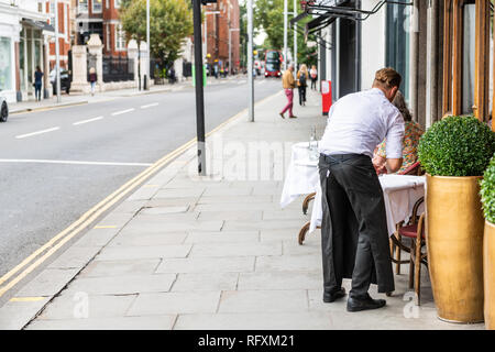 Londres, Royaume-Uni - 16 septembre 2018 : waiter standing mise en place cafe table à Chelsea à l'extérieur du trottoir de la rue restaurant pendant la journée Banque D'Images