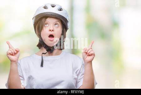 Les jeunes cyclistes adultes femme avec le syndrome de porter un casque de sécurité sur fond isolé dans l'étonnement et la surprise à la recherche avec les doigts pointant vers le haut et Banque D'Images