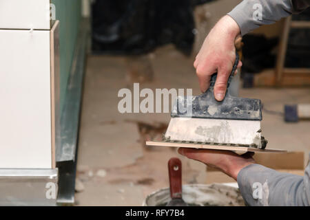 La main libre de constructeur ciment colle sur le frottis en carreaux de céramique avec une truelle pour colle dans la salle de bains privative. Concept Rénovation Réparation, révision, contrat carreleur Banque D'Images