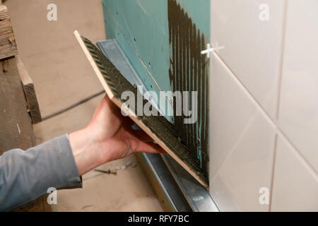 Libre constructeur professionnel de la main de l'homme de colles en carreaux de céramique avec de l'adhésif dans la salle de bains. Concept Rénovation Réparation, révision, carreleur, contrat de l'équipe Banque D'Images