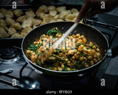 En remuant la main de pois chiches au curry indien et les épinards dans le wok cuisinière à gaz à l'intérieur. Banque D'Images