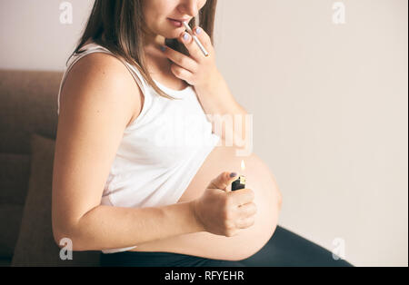 Portrait de briquet et l'allume en mains de femme enceinte. Femme en chemise blanche de fumer pendant la grossesse. Notion de menace et nuisibles Banque D'Images