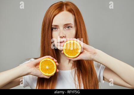 Fille avec deux moitiés d'oranges s sur fond gris Banque D'Images