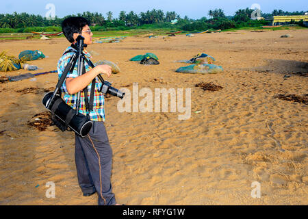 Un jeune garçon touristiques Bengali avec appareil photo et accessoires regardant la scène sur une plage de la mer with copy space Banque D'Images