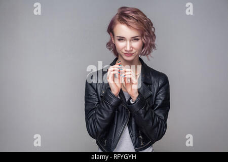 Portrait de cheater belle fille avec courte coiffure, maquillage dans style casual veste en cuir noire debout avec ruse et à la caméra à l'idée. Banque D'Images