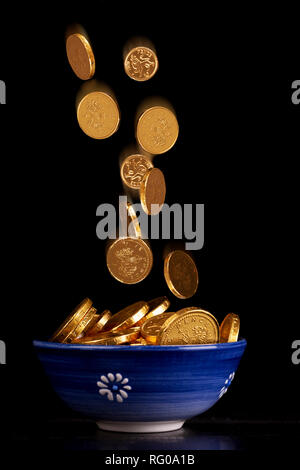 Pot d'or concept avec pièces d'or tombant dans le chocolat dans une casserole sur un fond noir Banque D'Images