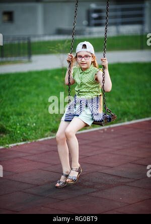 Jeune fille sérieuse sur l'oscillation. Enfant dans l'aire de jeux. Focus sélectif. Banque D'Images