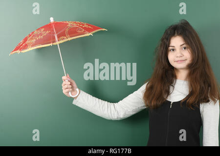 Smiling little schoolgirl sur fond vert . Jeune fille espiègle est titulaire d'un parapluie rouge dans sa main Banque D'Images