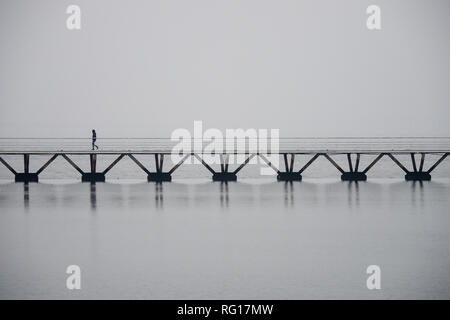 Homme seul marche sur un pont au-dessus de l'eau à Lisbonne, atmosphère brumeuse, copyspace Banque D'Images