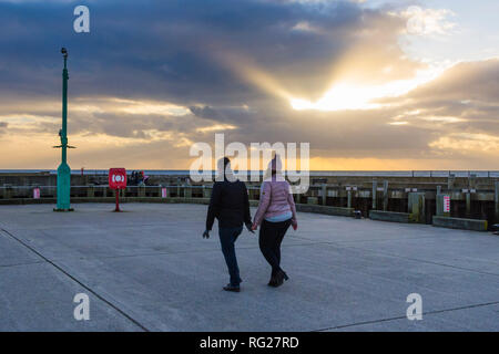 West Bay, Dorset, UK. 27 janvier 2019. Météo britannique. Un couple en train de marcher le long de la jetée que poutres du soleil à travers les nuages au-dessus de la baie de l'Ouest dans le Dorset par une froide après-midi breezy Photo Credit : Graham Hunt/Alamy Live News Banque D'Images