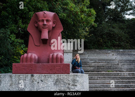 Femme, l'utilisation de smartphone, assise à côté de terre cuite peinte sphinx, partie de la grande terrasse, Crystal Palace, London, England, UK Banque D'Images