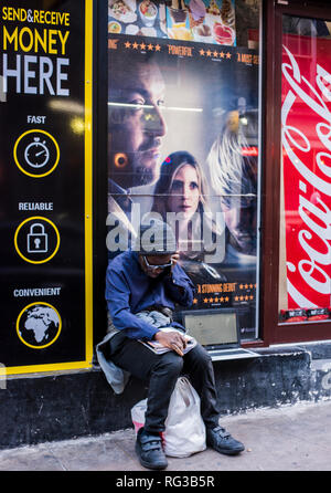 Homme assis sur le mur, des affiches publicitaires dans la fenêtre derrière lui, à l'aide d'un ordinateur portable, smartphone sur le mur à côté de lui, le centre de Londres, Angleterre, RU Banque D'Images