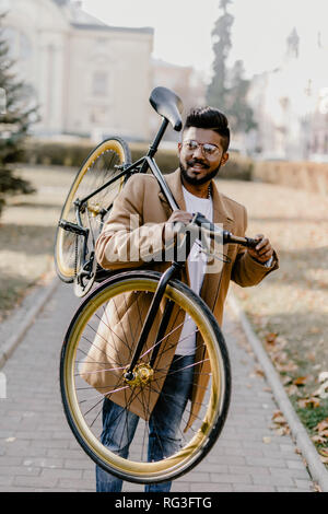 Homme barbu hippie indien avec un fixie vélo. Low angle view of certain jeune homme barbu portant son vélo sur l'épaule et looking at camera Banque D'Images