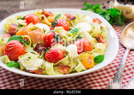 Pâtes fettuccine cuits au four avec tomates, bacon et fromage mozzarella sur fond de bois rustique. Focus sélectif. Banque D'Images