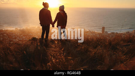 Silhouette de jeune homme et de la femme de l'amour debout sur le sommet de la montagne se tenant la main et se regardant avec seascape en arrière-plan. Romantic Banque D'Images