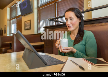 Lit ce que blogger femelle elle a tapé sur sa tablette tout en tenant une tasse de café. Assis seul sur un stand axé sur l'écran tandis que le café. Banque D'Images