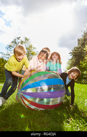 Groupe d'enfants joue hilariously avec une boule colorée dans le parc de vacances d'été Banque D'Images