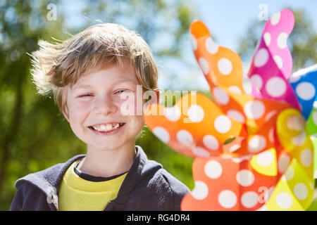 Naughty smiling boy avec un moulinet multicolore en été au soleil Banque D'Images
