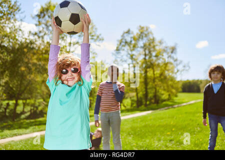 Fille joue au football avec des amis sur un pré à l'été et tient fièrement la balle Banque D'Images