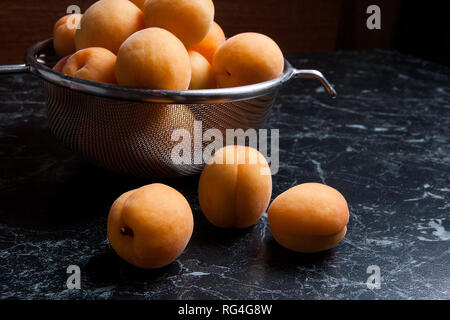 Organique mûres les abricots dans une passoire en acier. Composition dans un style rustique - jaune bio abricots juteux dans son ensemble et passoire en acier et des moitiés d'abricots o Banque D'Images