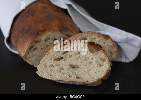 Pain au levain cuit juste - la qualité rustique enveloppée dans une serviette de table fait maison avec des tranches de pain allongé. Belle ville pittoresque close up image avec selectiv Banque D'Images