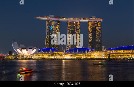 Marina Bay Sands Hotel avec deux touristes bateaux dans l'eau en face de l'hôtel ; la photographie de nuit avec une longue exposition, juste avant la nuit, à Singapour. Banque D'Images