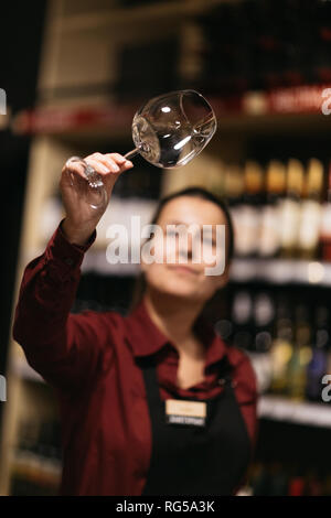 Photo de femme avec un verre de vin sur fond flou d'étagères avec des bouteilles Banque D'Images