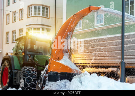 Grand tracteur avec des chaînes sur les roues de la poudrerie à partir de la rue de ville en dump truck body. Le nettoyage des rues et l'enlèvement de la neige après chute de neige. Services municipaux Banque D'Images