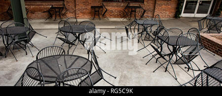 Coin salon extérieur fermé d'un restaurant avec chaises fer urbains mis en place appuyé contre les tables. Banque D'Images