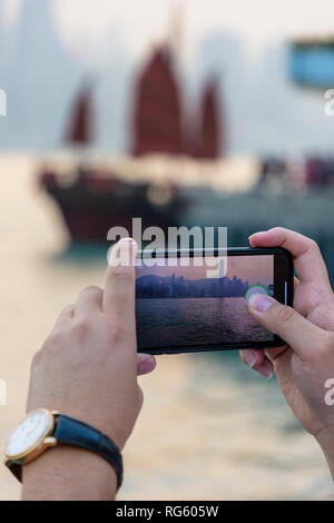 Prenant une photo touristique sur son téléphone mobile de l'horizon de Hong Kong au coucher du soleil, le port de Victoria, Hong Kong Banque D'Images