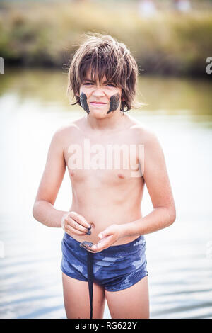 Boy standing in Atanasovsko Lake mettant de la boue sur son visage, Burgas, Bulgarie Banque D'Images