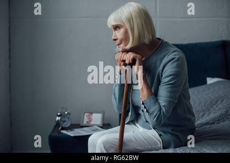 Lonely Woman with hands on walking stick assis sur le lit à la maison Banque D'Images