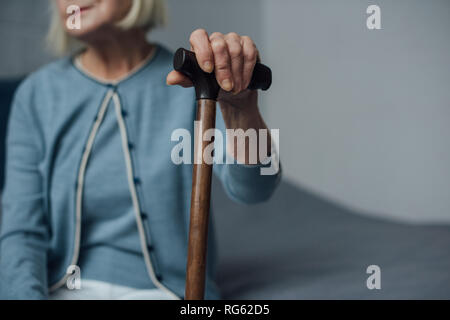 Vue partielle de senior woman sitting on bed holding et bâton de marche à la maison Banque D'Images