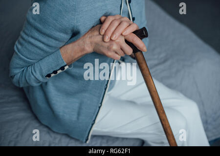 Portrait of senior woman sitting on bed avec bâton de marche à la maison Banque D'Images