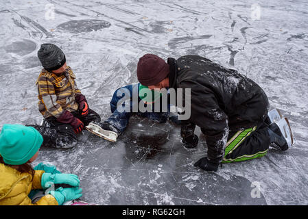 Père et trois enfants assis sur un lac gelé à la recherche à travers la glace, United States Banque D'Images