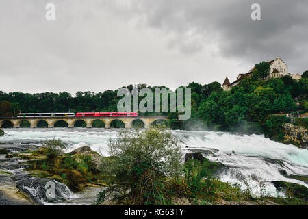 Train rouge sur le pont ferroviaire aux chutes du Rhin (Rheinfall). Rhinefall est la plus grande cascade d'Europe. Situé dans le Haut-Rhin, Neuhausen, Schaffhausen, Banque D'Images