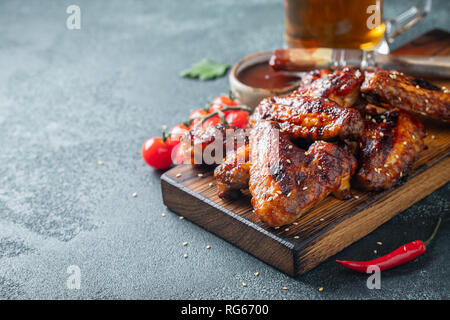 Ailes de poulet grillées au barbecue, sauce aux graines de sésame et le persil sur une planche en bois sur une table en béton. Avec l'exemplaire de l'espace. Délicieux en-cas pour la bière sur Banque D'Images