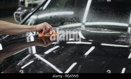Film de protection pour l'application professionnelle la voiture rouge. Colles maître un film de protection sur le capot de la voiture Banque D'Images