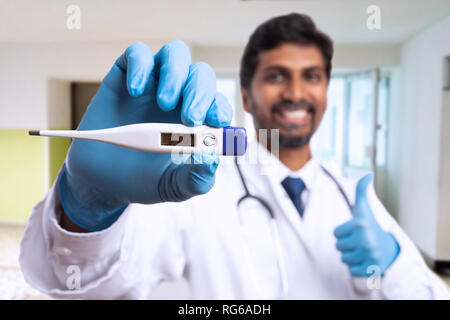 L'accent image en gros plan de thermomètre tenu par indian medic ou médecin showing thumb-up comme comme geste et souriant de couloir de l'hôpital comme arrière-plan Banque D'Images