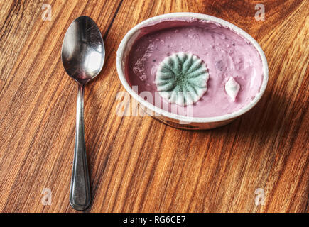 Yaourt aux fruits pourris avec de belles colonies de champignons de moisissure. Tasse en plastique, acier inoxydable cuillère à café sur table en bois. Banque D'Images