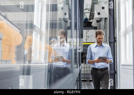 Businessman checking robots avec tablette numérique dans la société de haute technologie Banque D'Images