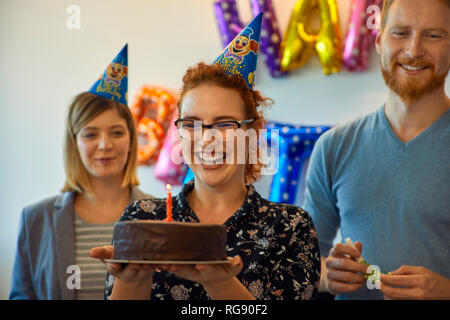 Des collègues ayant un bureau en célébration d'anniversaire avec gâteau et chapeaux de fête Banque D'Images
