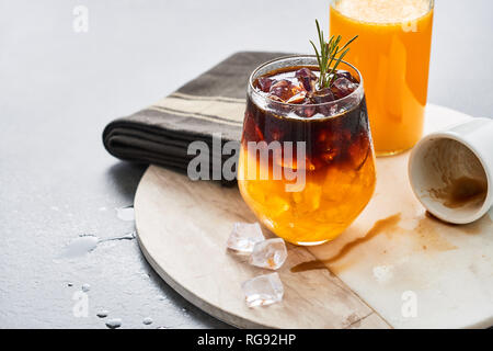 Froid de glace boisson d'été. Expresso jus d'orange avec de la glace, une bouteille de jus d'orange bio et vide d'espresso sur une assiette de marbre blanc sur noir Banque D'Images