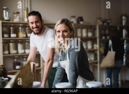 Un portrait de deux assistants boutique joyeux debout dans zéro déchets boutique, looking at camera. Banque D'Images