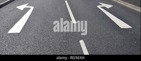 Décision choix concept avenir changement de direction au milieu du choix de la route tourner à gauche et à droite des flèches sur la ligne droite noir options tarmac England UK Banque D'Images